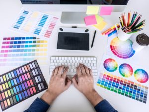 Image of male creative graphic designer working on color selection and drawing on graphics tablet at workplace with work tools and accessories, top view workspace.