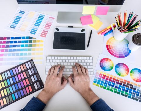 Image of male creative graphic designer working on color selection and drawing on graphics tablet at workplace with work tools and accessories, top view workspace.